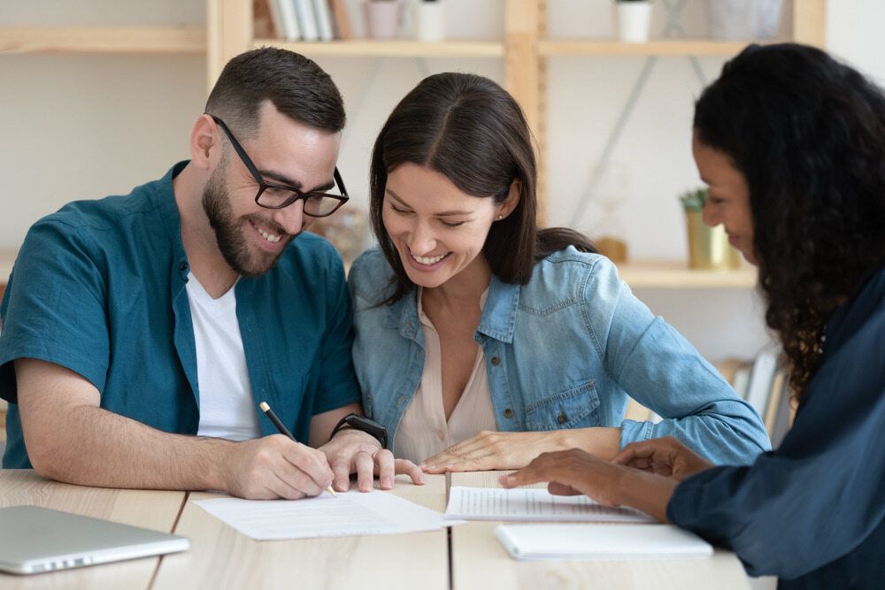 A Man and a Woman Are Sitting at a Table Signing a Document — Key2 Conveyancing In Pacific Palms, NSW