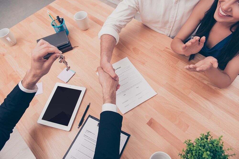 A Man is Shaking Hands With a Woman While Sitting at a Table — Key2 Conveyancing In Forster, NSW