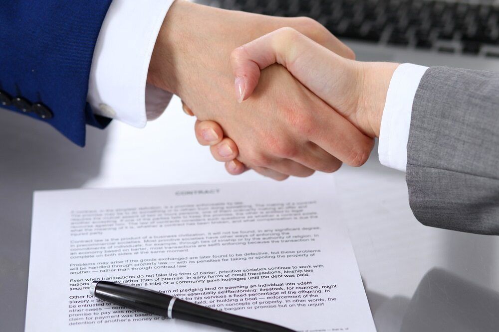 A Man and a Woman Are Shaking Hands Over a Contract — Key2 Conveyancing In Pacific Palms, NSW