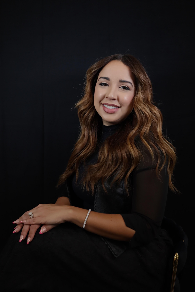 A woman in a black dress is sitting in a chair and smiling.