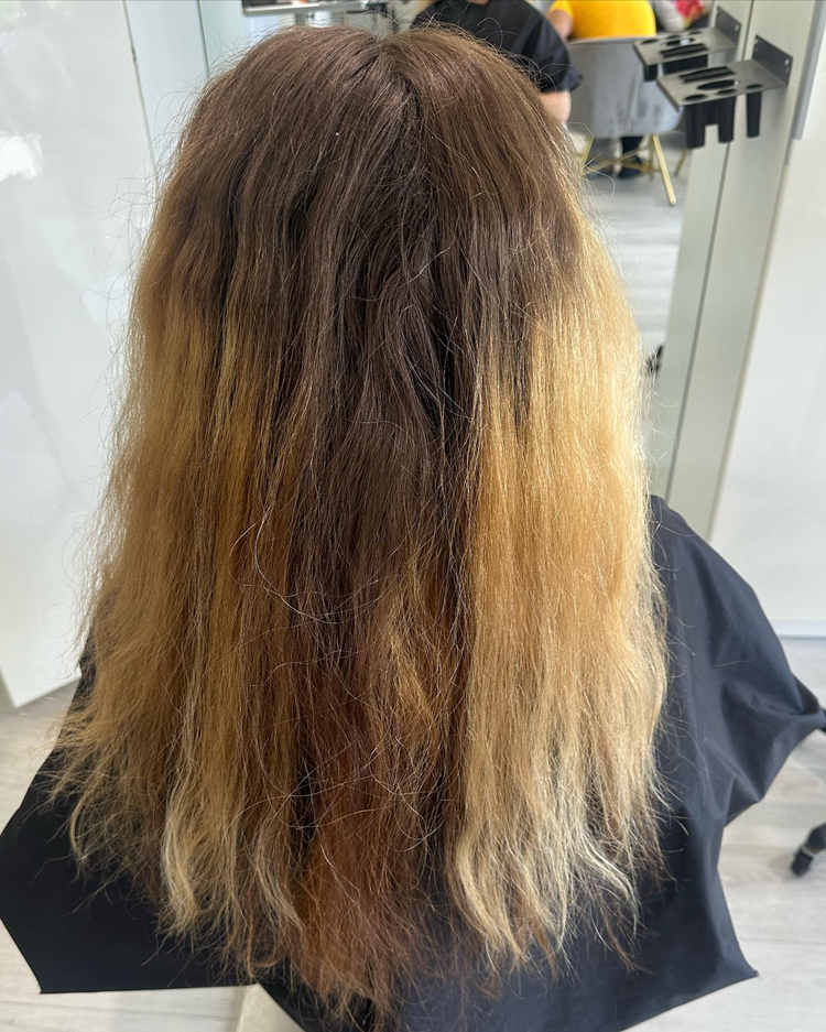 A woman with long hair is sitting in a chair in front of a mirror.