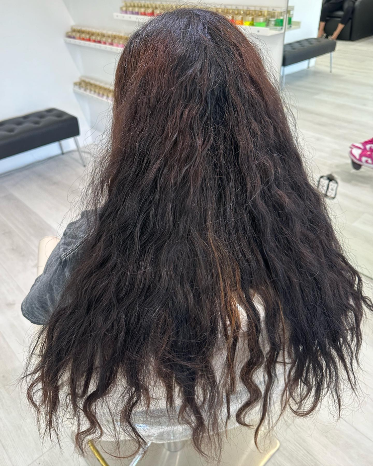 A woman with long dark hair is sitting in a chair in a salon.