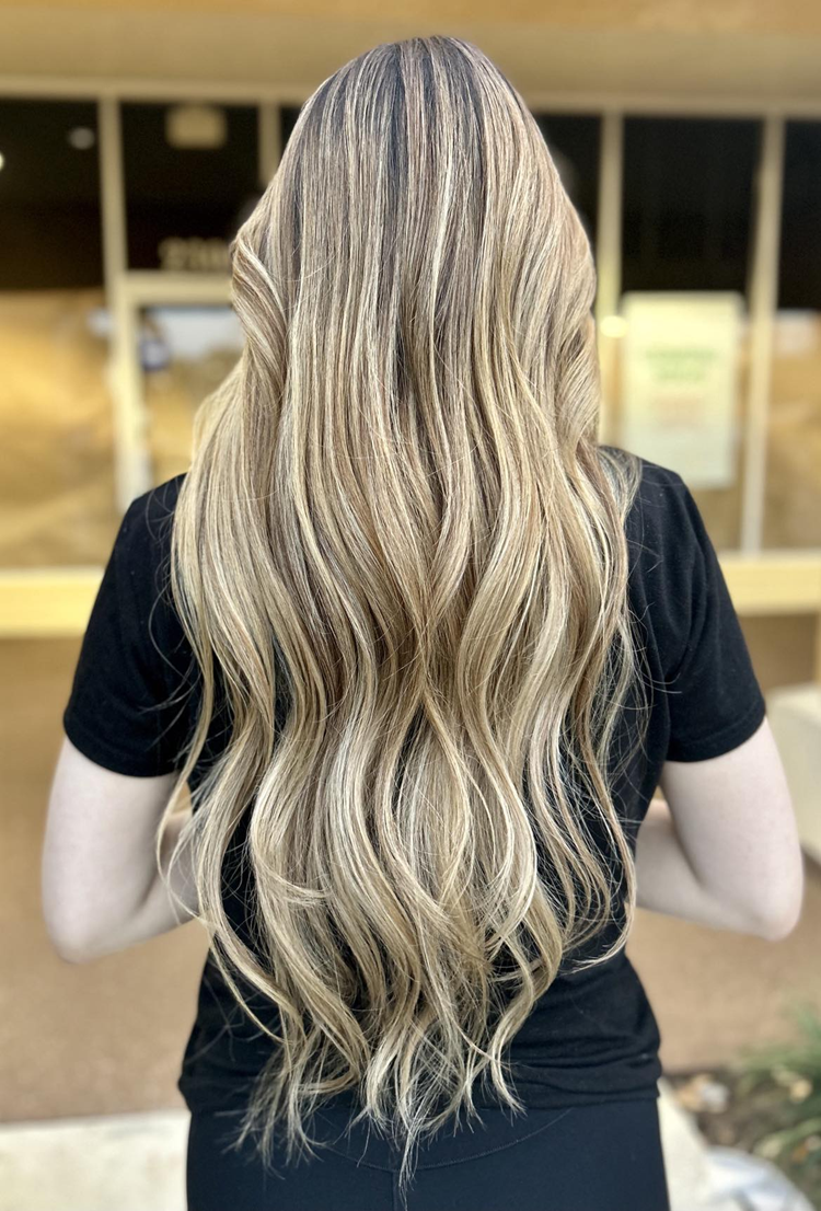 A woman with long blonde hair is wearing a black shirt and standing in front of a window.