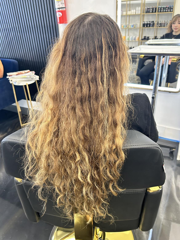 A woman with long curly hair is sitting in a chair in a salon.