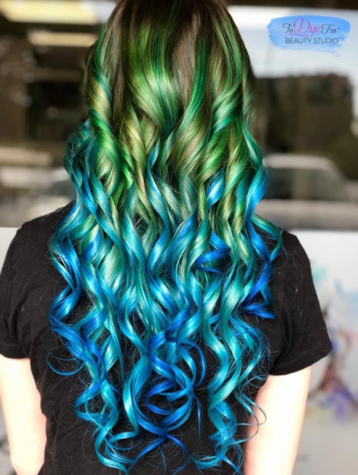 A woman with green and blue hair is wearing a black shirt.