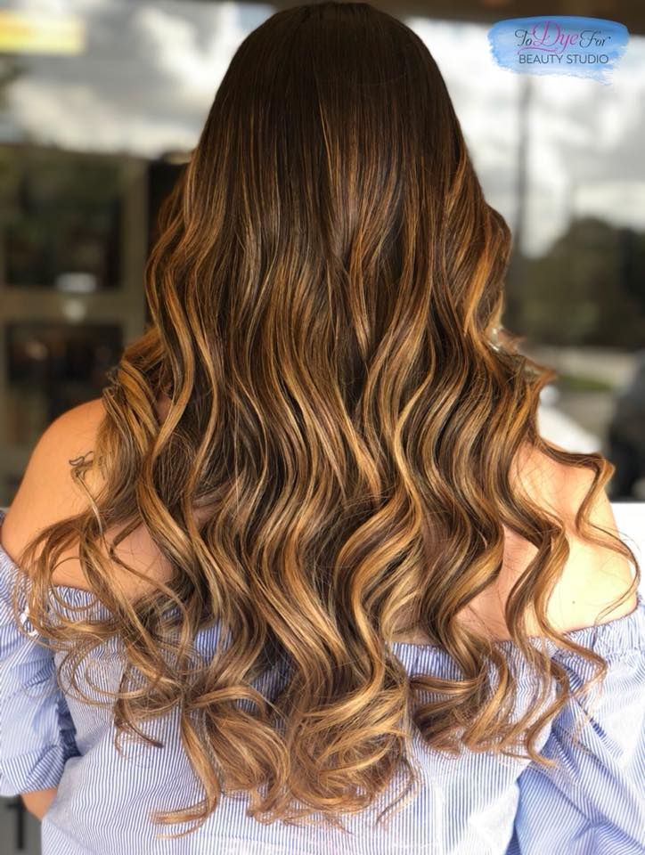 A woman with long wavy brown hair is wearing a blue off the shoulder top.
