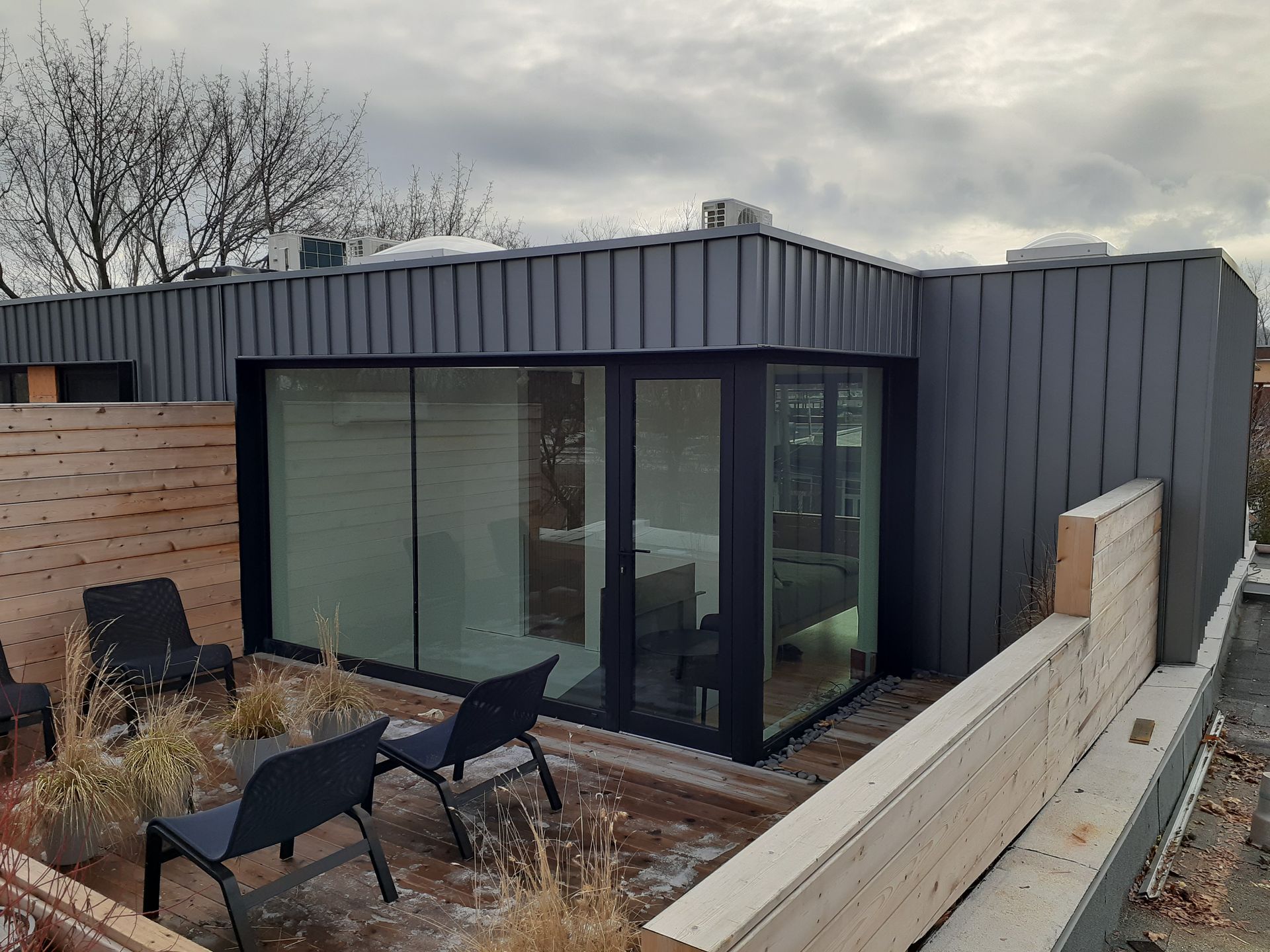 Une maison noire avec une grande fenêtre et des chaises sur le patio.