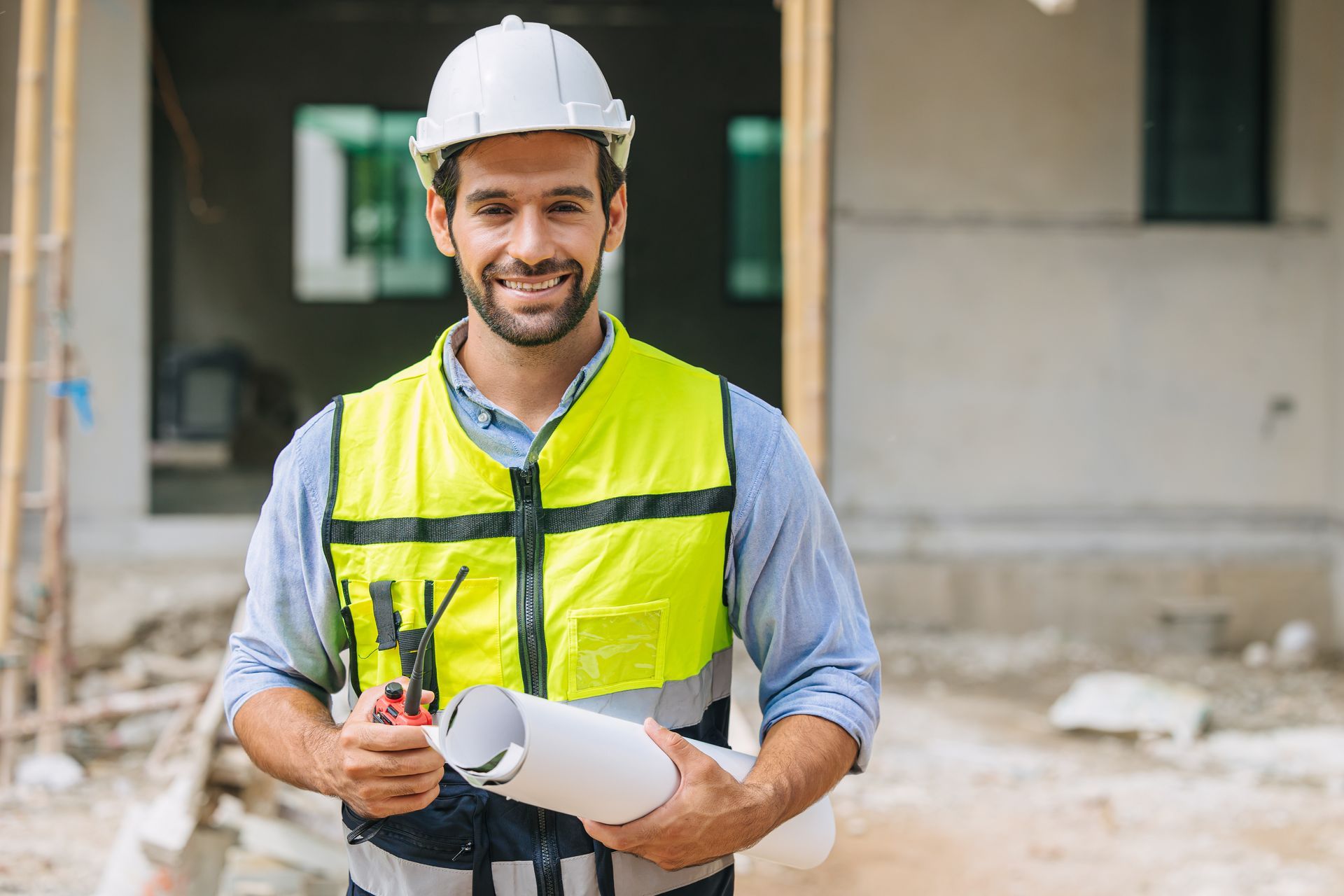 Un ouvrier du bâtiment tient un plan et sourit à la caméra.