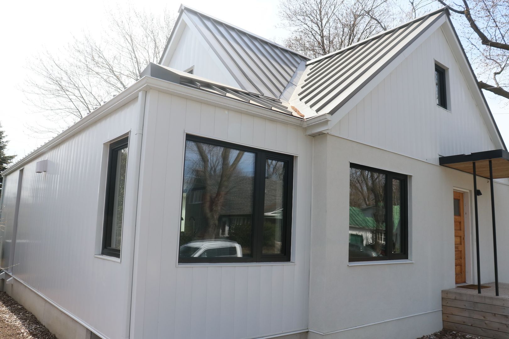 Une maison blanche avec des fenêtres noires et un toit en métal