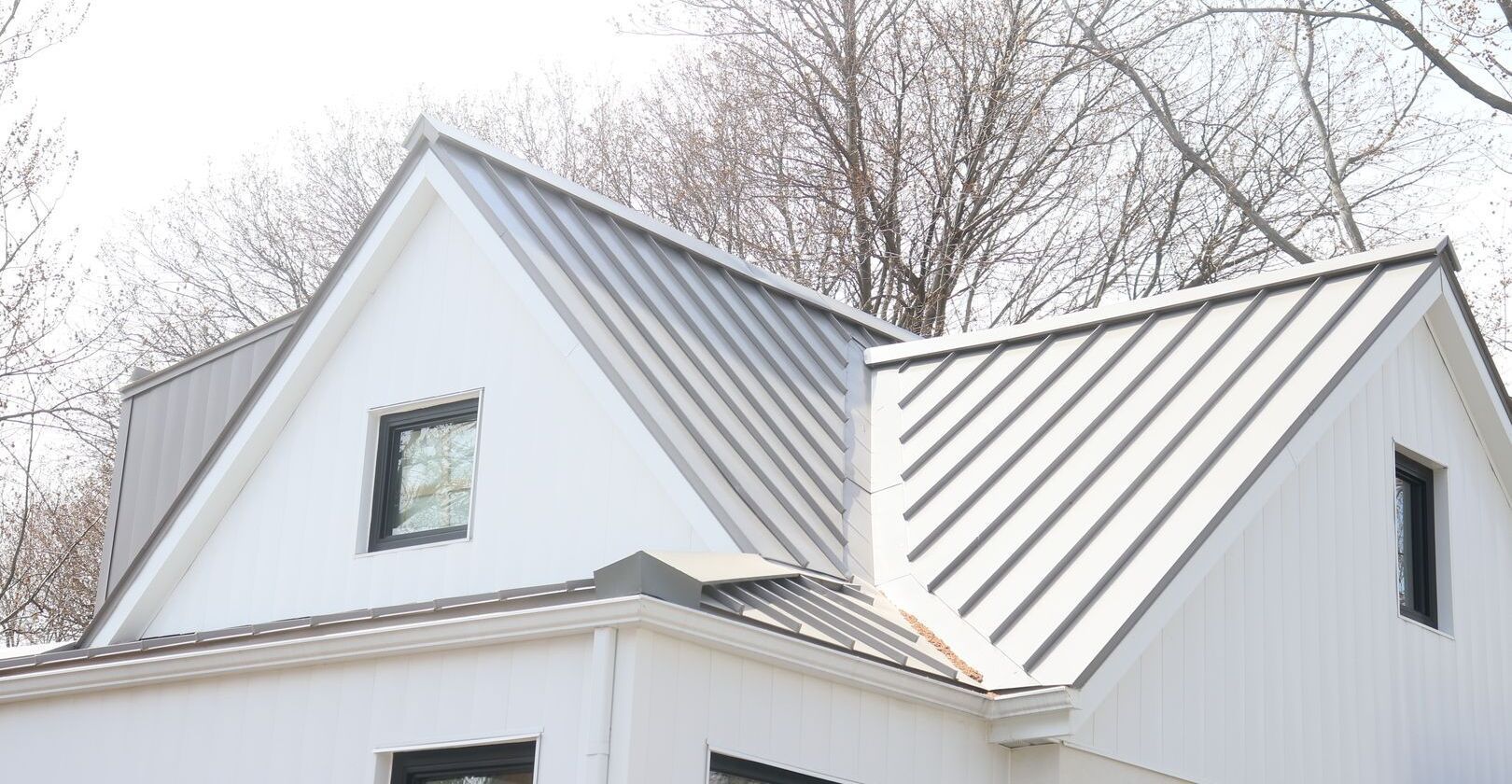 Une maison blanche avec un toit en métal et des arbres en arrière-plan.
