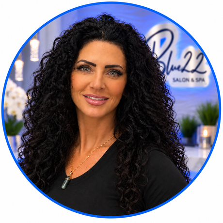 Blue 22 Salon & Spa Woman with curly dark hair posing in front of a salon spa sign