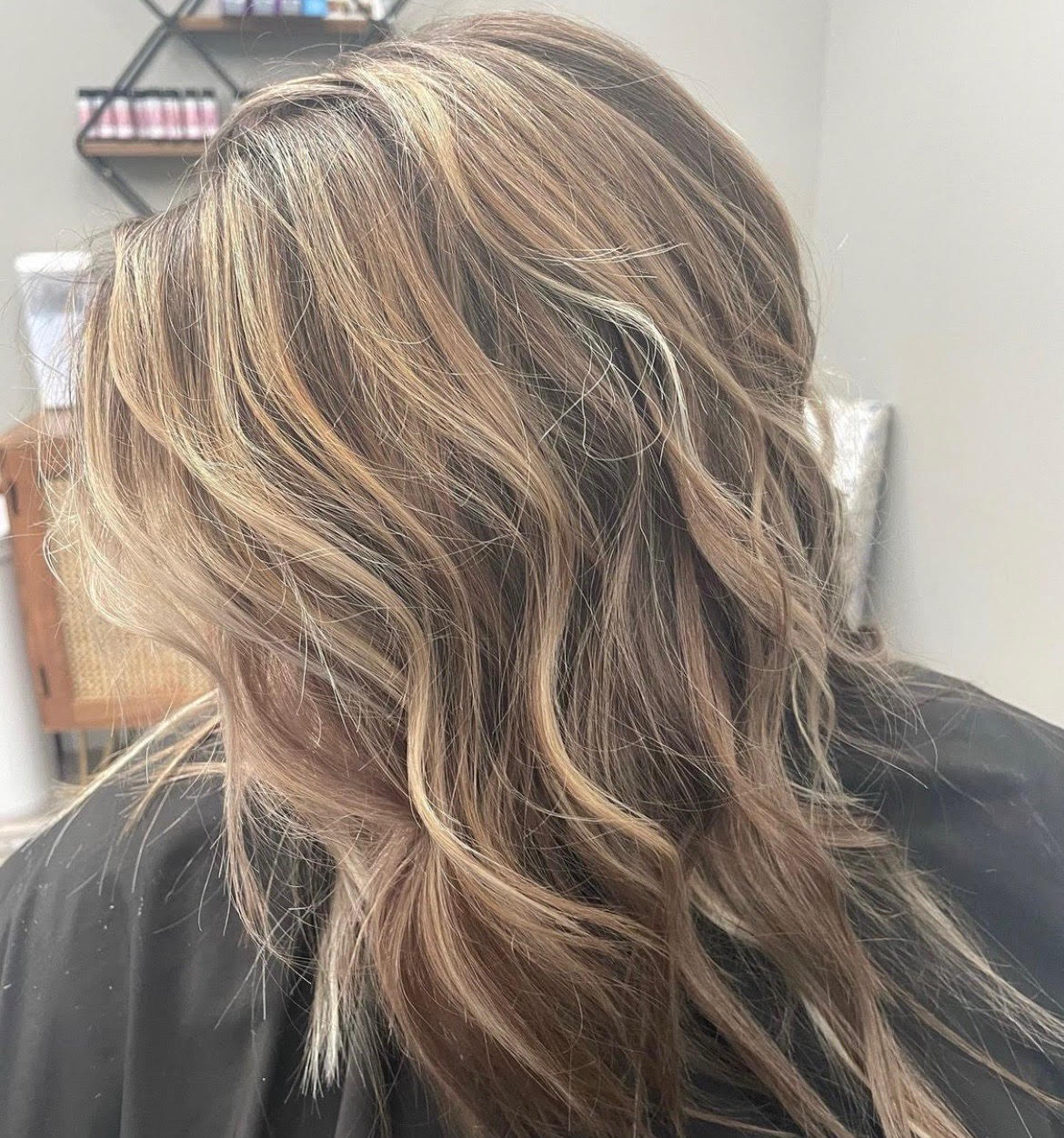 Wavy brown-highlighted hair styled in loose layers, seen from the back in a salon chair