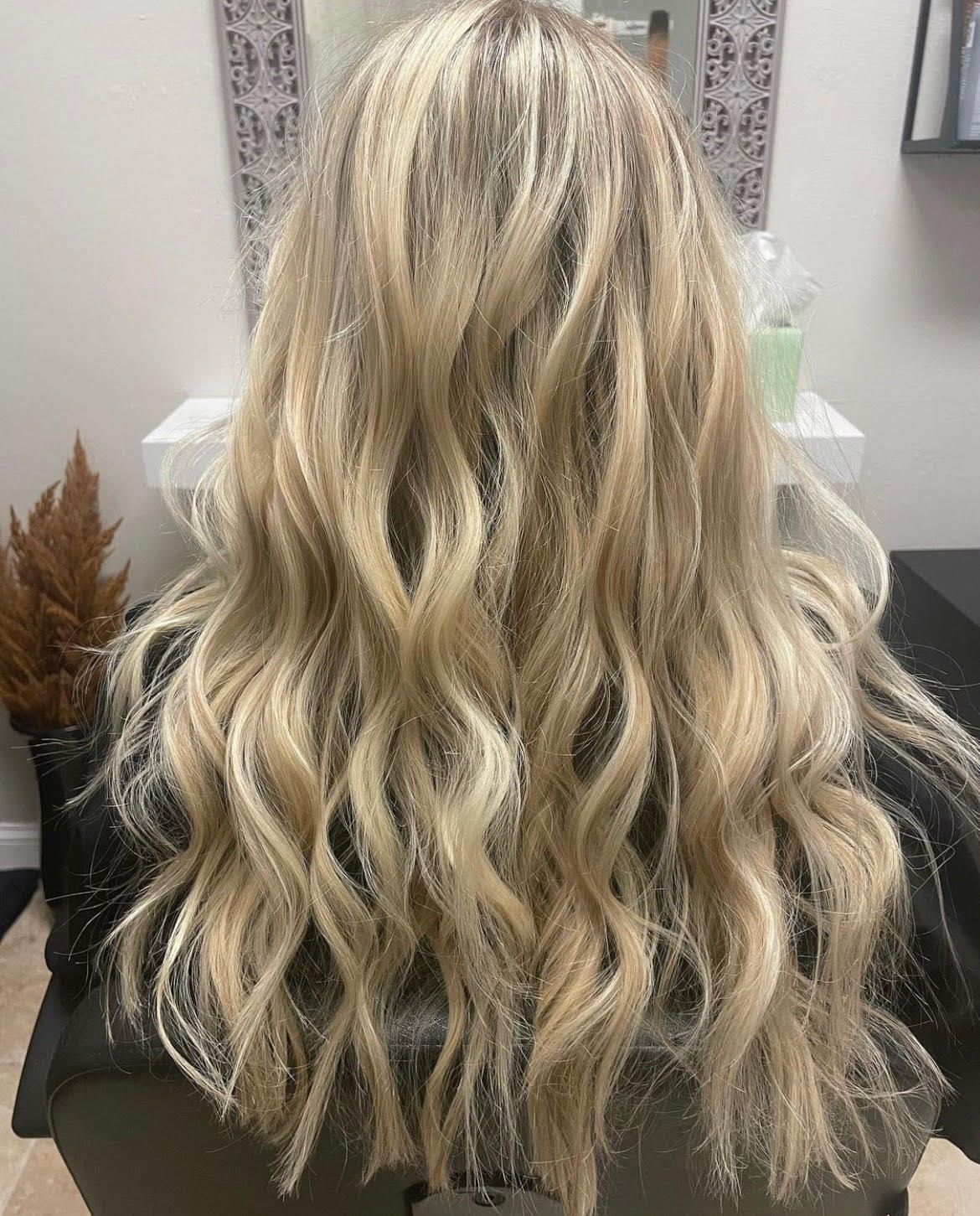 Long wavy blonde hair with darker roots, styled in loose waves from the back.