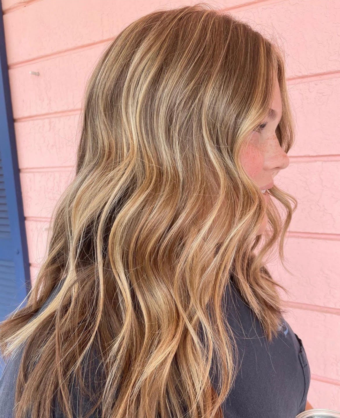 Blue 22 Salon & Spa Side view of a person with wavy blonde hair against a pink wall