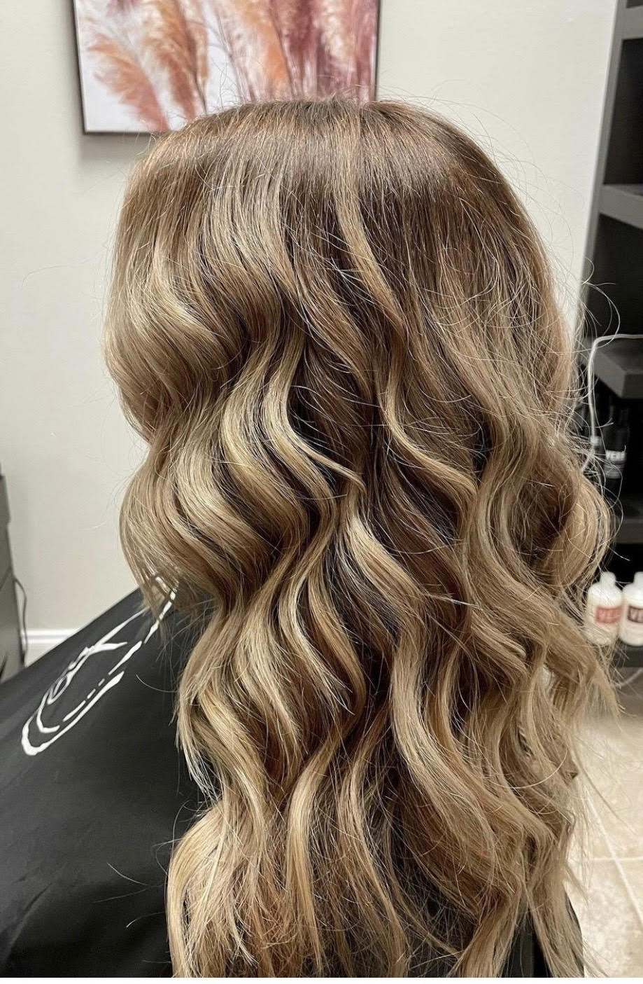 Long wavy brunette hair with blonde highlights, styled in loose curls from the back view.