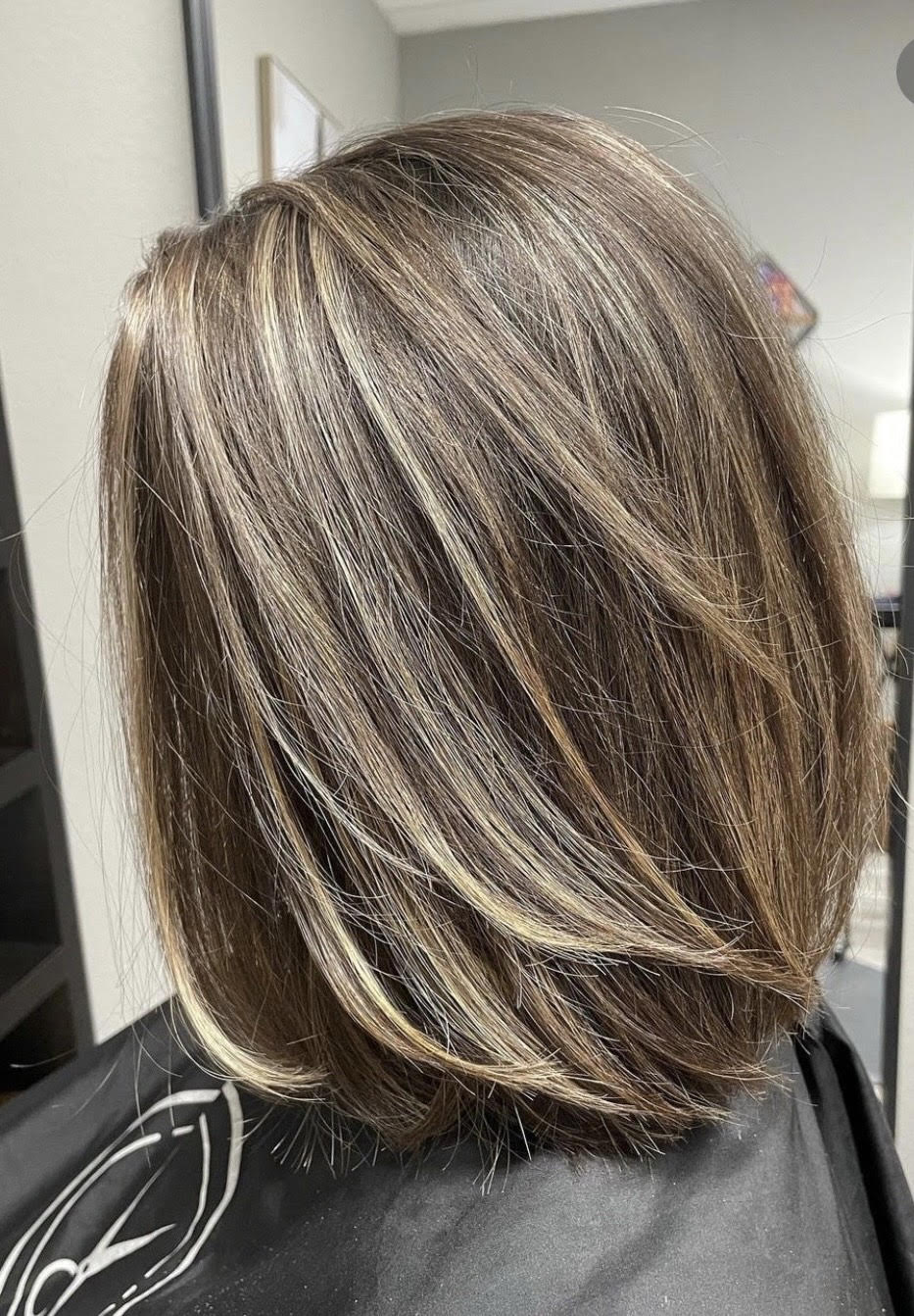 Short layered brown bob with blonde highlights, shown from the back in a salon chair