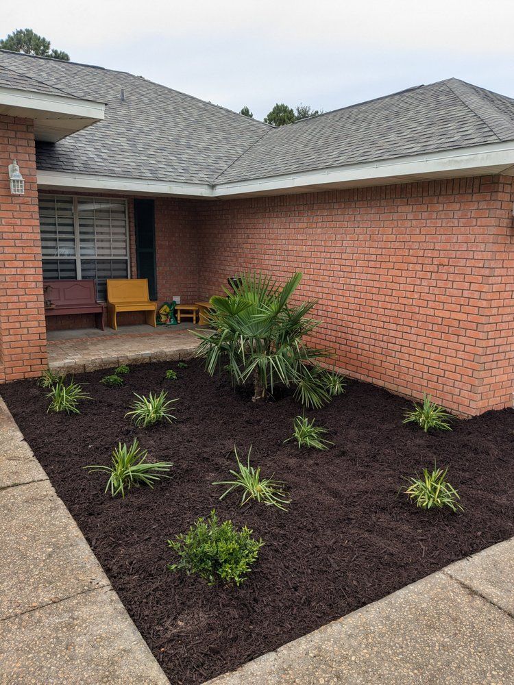 Brick house courtyard with new mulch bed and small green plants under a gray shingled roof.