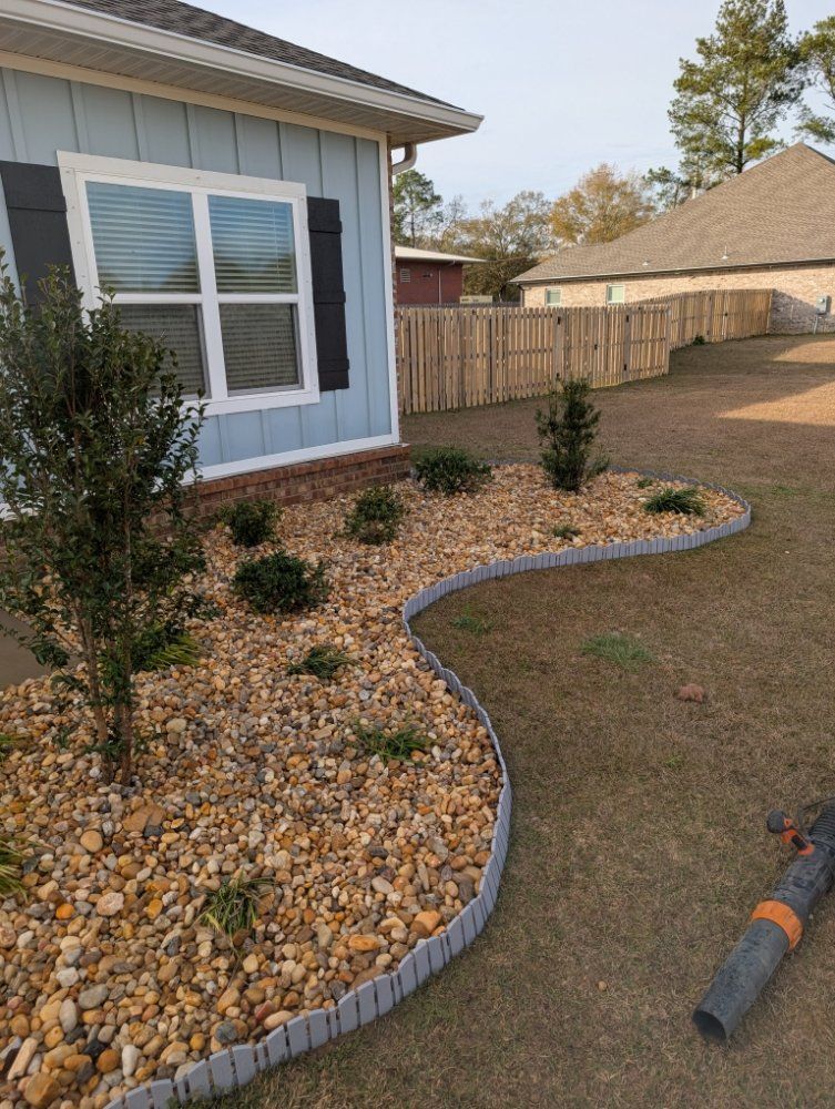 Curved stone-edged landscaping bed with shrubs beside a house, bordered by mulch and lawn