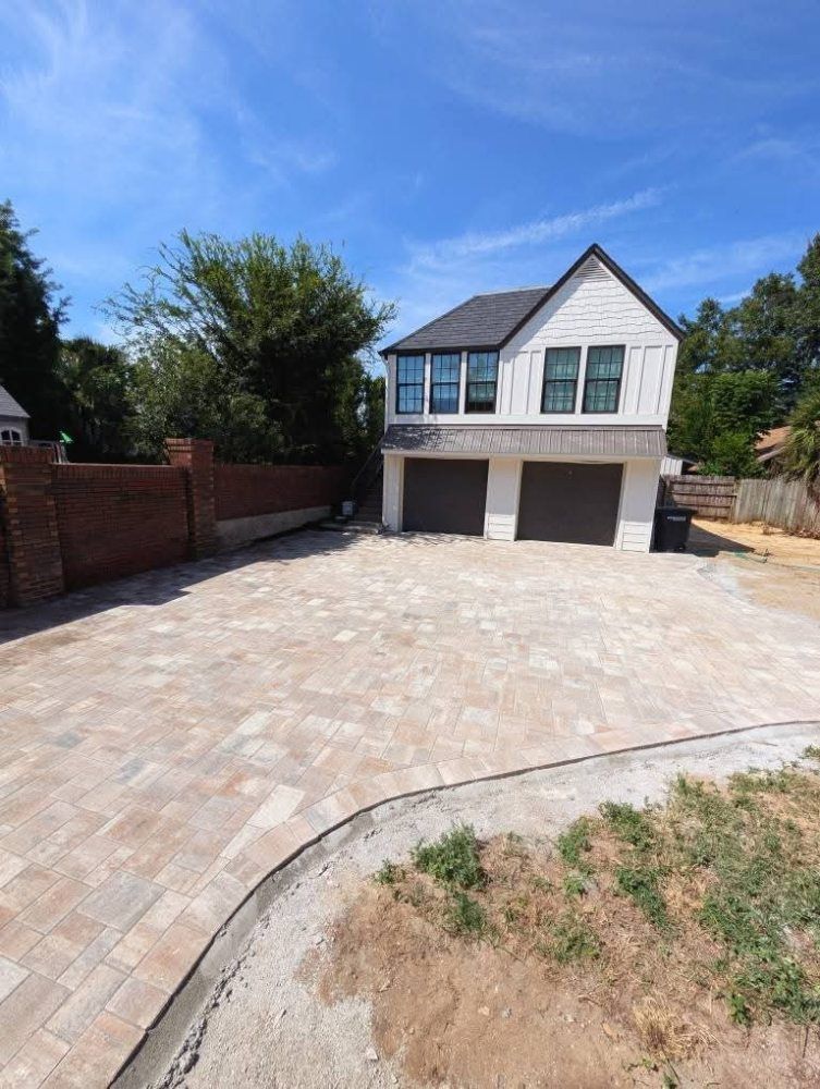 Wide paved driveway leading to a two-story house with a double garage under a blue sky