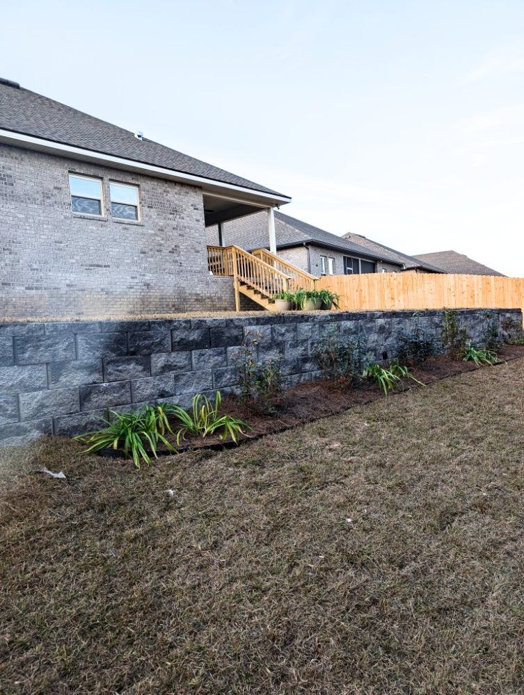 Suburban house with stone retaining wall, wooden stairs, and a fenced yard on a sloped lawn.