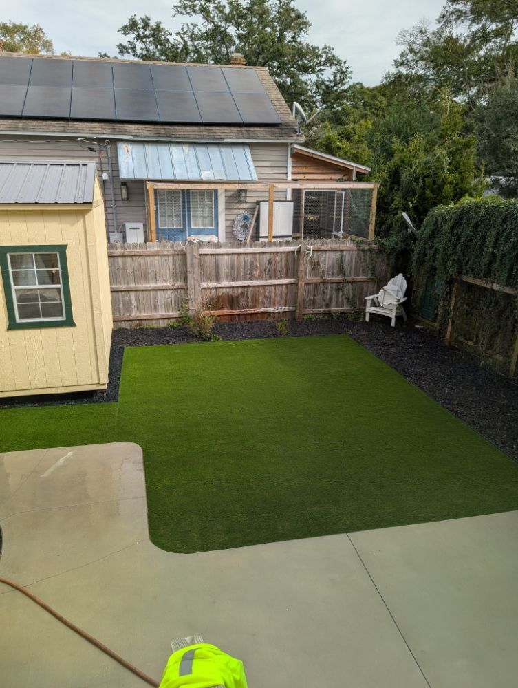 Backyard with artificial grass, concrete patio, shed, fenced seating area, and solar panels on the roof