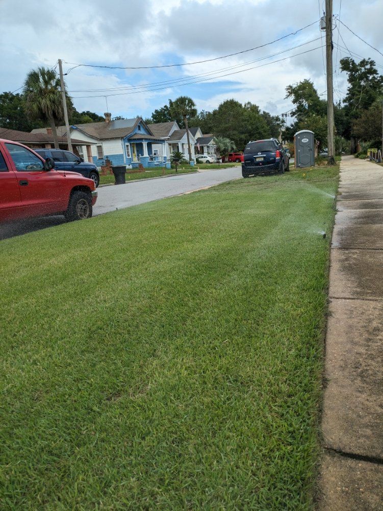 Suburban street with parked cars, grassy verge, sidewalk, and houses under a cloudy sky