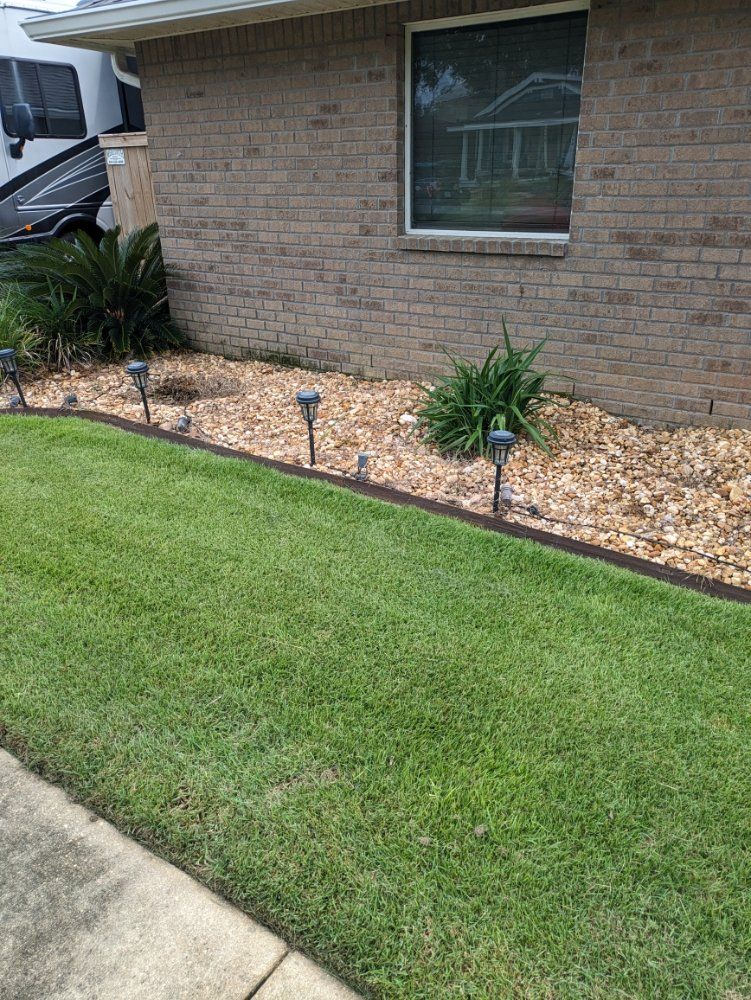 Brick house front yard with green lawn, stone mulch bed, and small shrubs along the wall