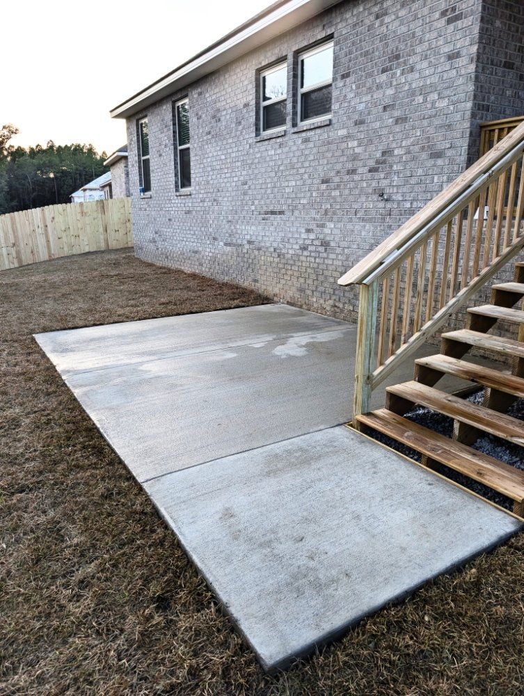 Concrete patio beside a house with a wooden staircase and white brick exterior.