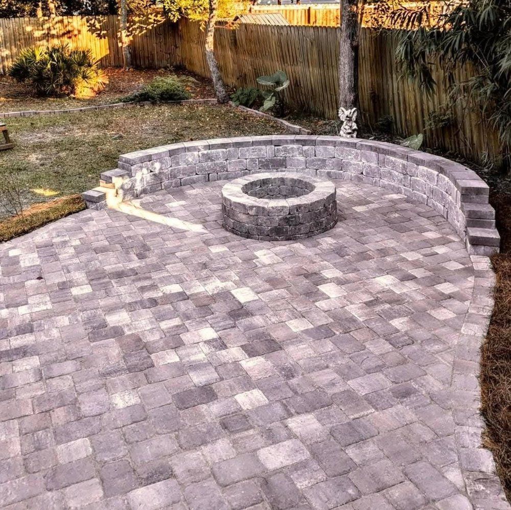 Curved stone-paver patio with a circular fire pit and low retaining wall in a backyard