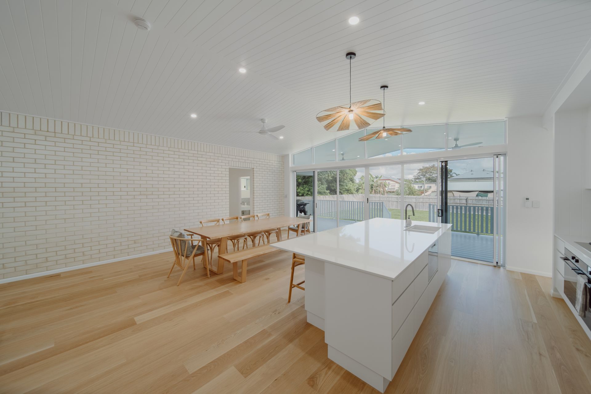Bright Kitchen With White Cabinets, Wooden Floors, Dining Table, And Large Sliding Doors — Simon Bell Constructions in Alice River, QLD
