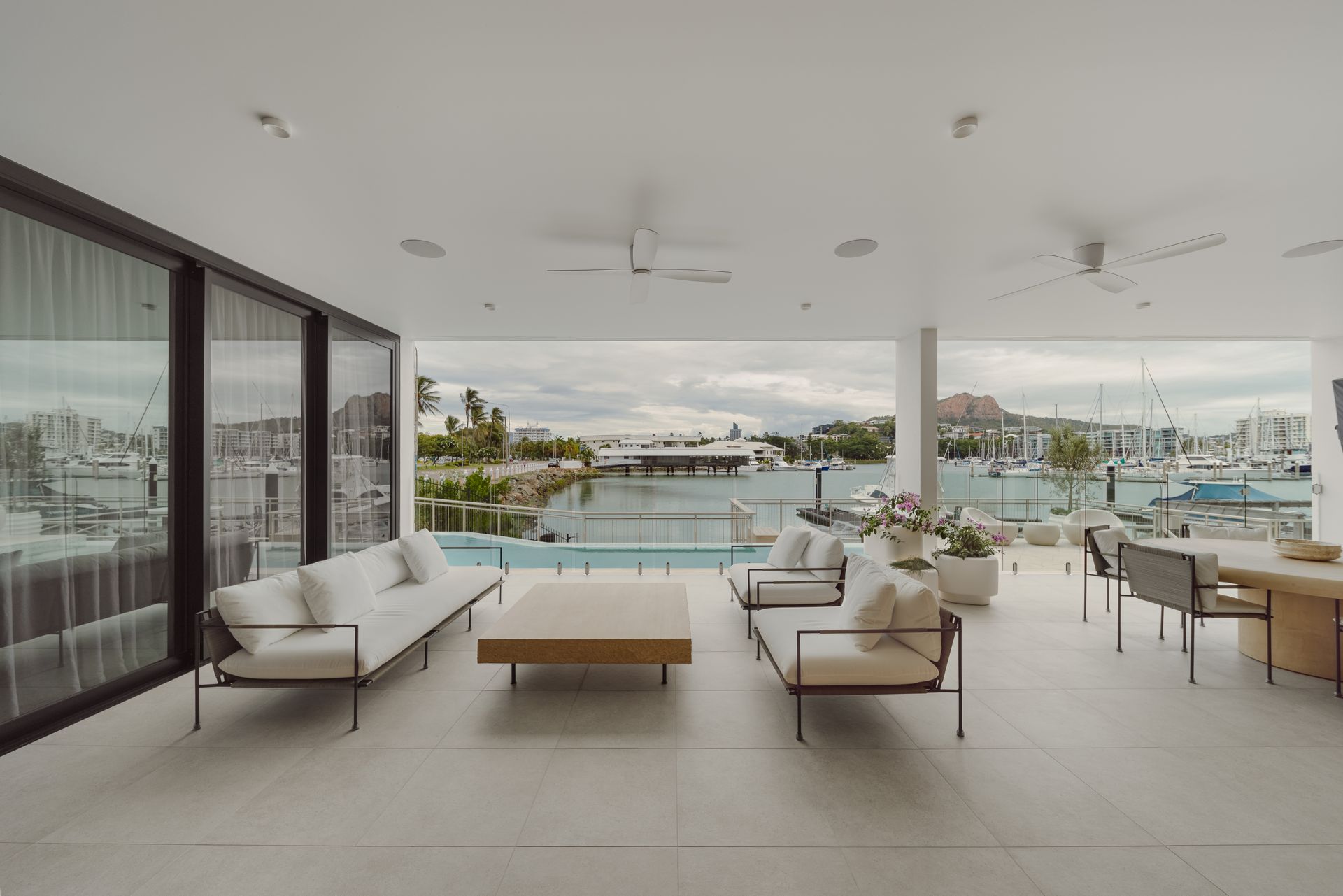 Open-air Patio Overlooking Water And Boats; White Sofas, Square Wooden Coffee Table, Dining Table — Simon Bell Constructions in Alice River, QLD