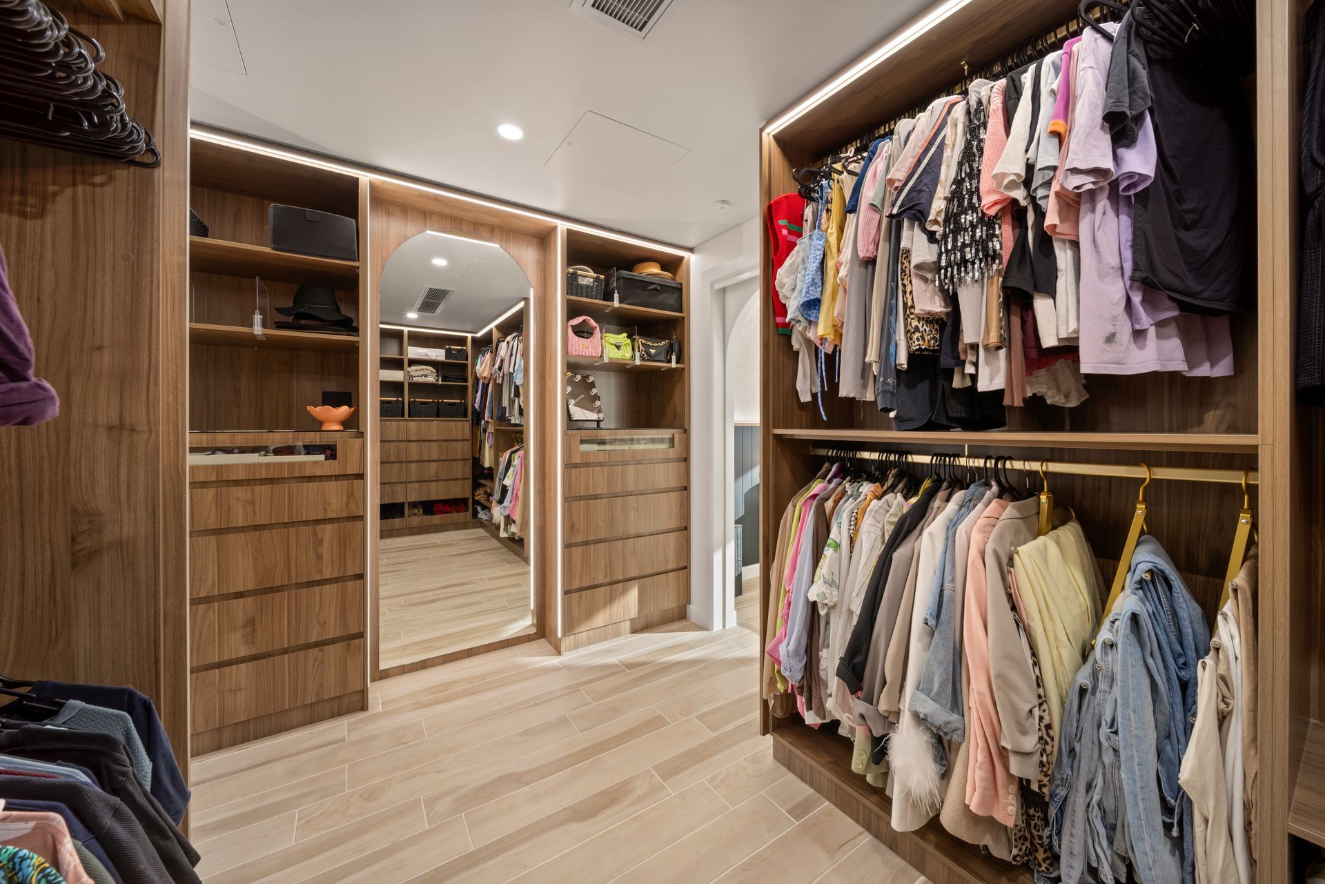 Modern Walk-in Closet With Clothes Hanging on Both Sides and Mirrored Sliding Doors in the Center — Simon Bell Constructions in Alice River, QLD