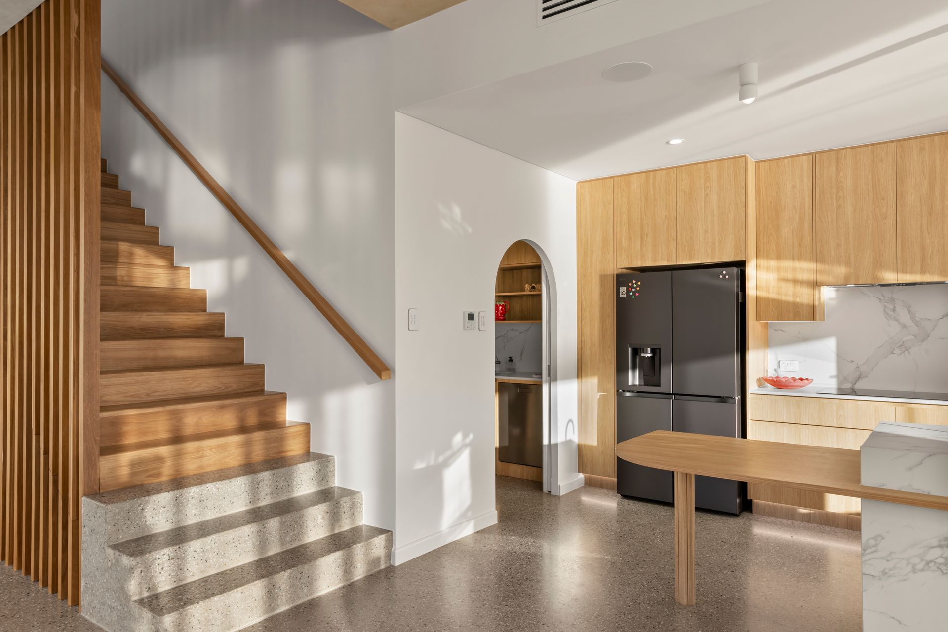 Modern Kitchen With Wood Cabinets, Black Fridge, Staircase — Simon Bell Constructions in Alice River, QLD