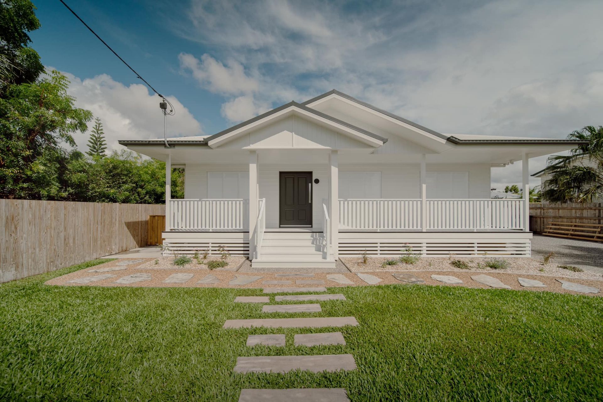 White House With A Porch, Fronted By A Stone Path And Green Lawn Under A Partly Cloudy Sky — Simon Bell Constructions in Alice River, QLD