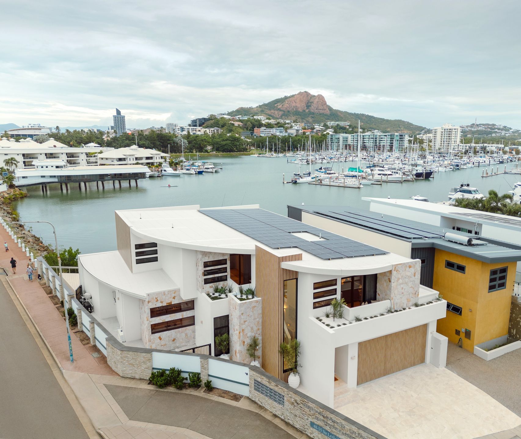 Modern White Home With Solar Panels, Overlooking A Marina And A Hill On An Overcast Day — Simon Bell Constructions in Alice River, QLD
