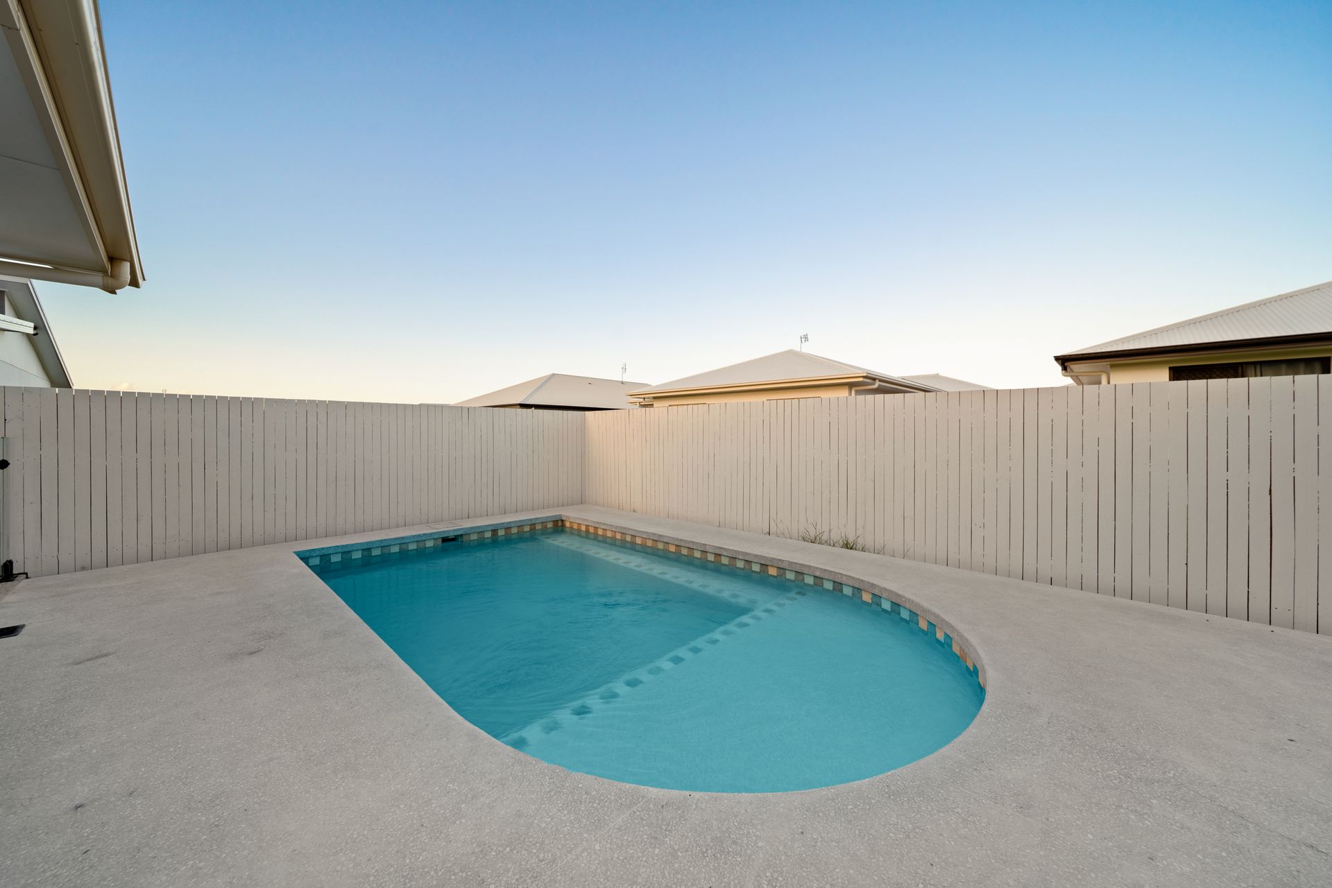 Empty Backyard Pool With Blue Water, Surrounded by a White Fence and Concrete Patio — Simon Bell Constructions in Alice River, QLD