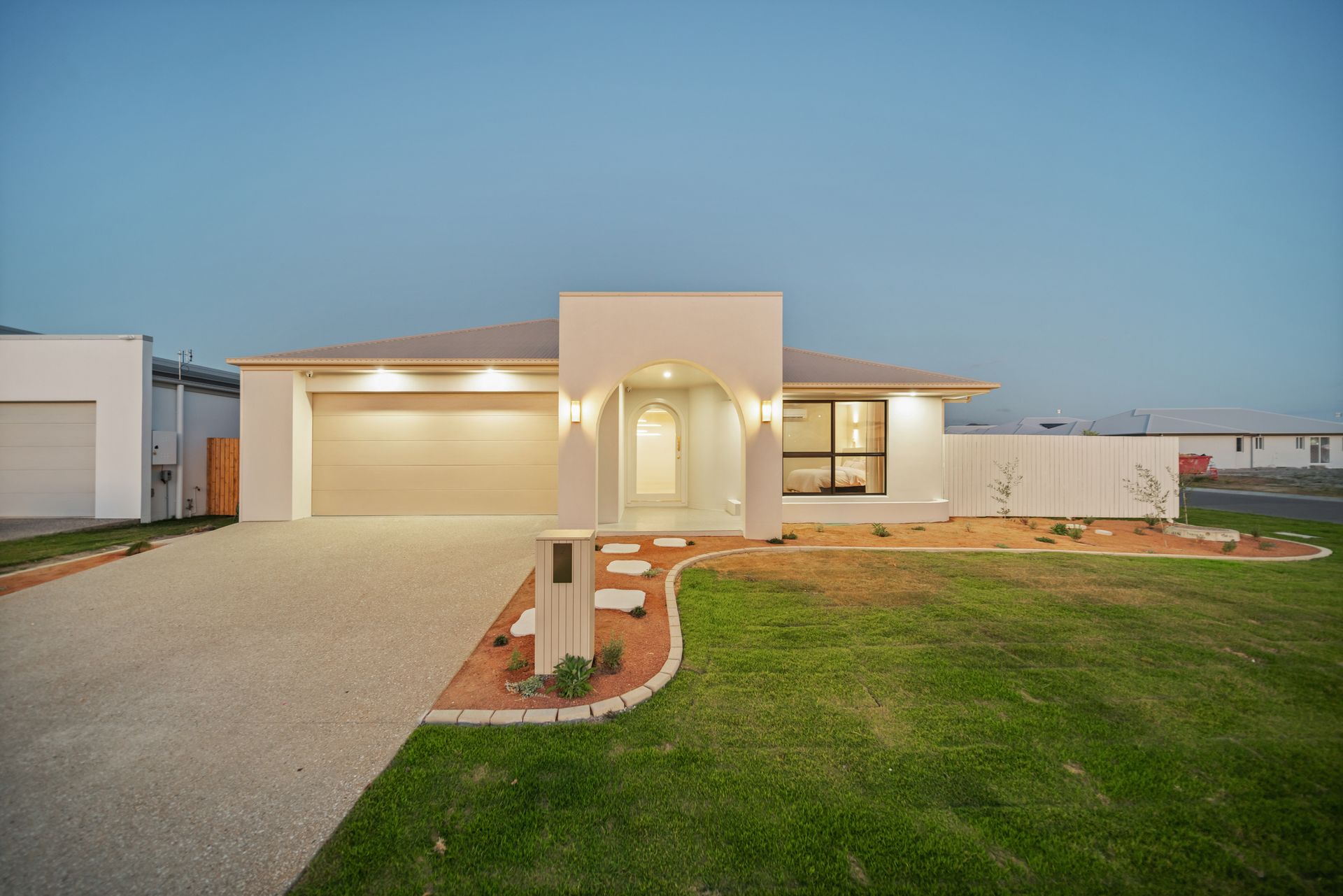 Modern Single-story House at Dusk With Lit Garage, Front Walkway, and Green Lawn — Simon Bell Constructions in Alice River, QLD