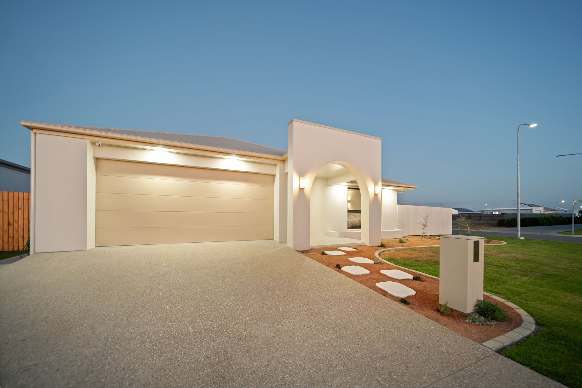 Modern White House With Lit Garage and Arched Entry at Dusk — Simon Bell Constructions in Alice River, QLD