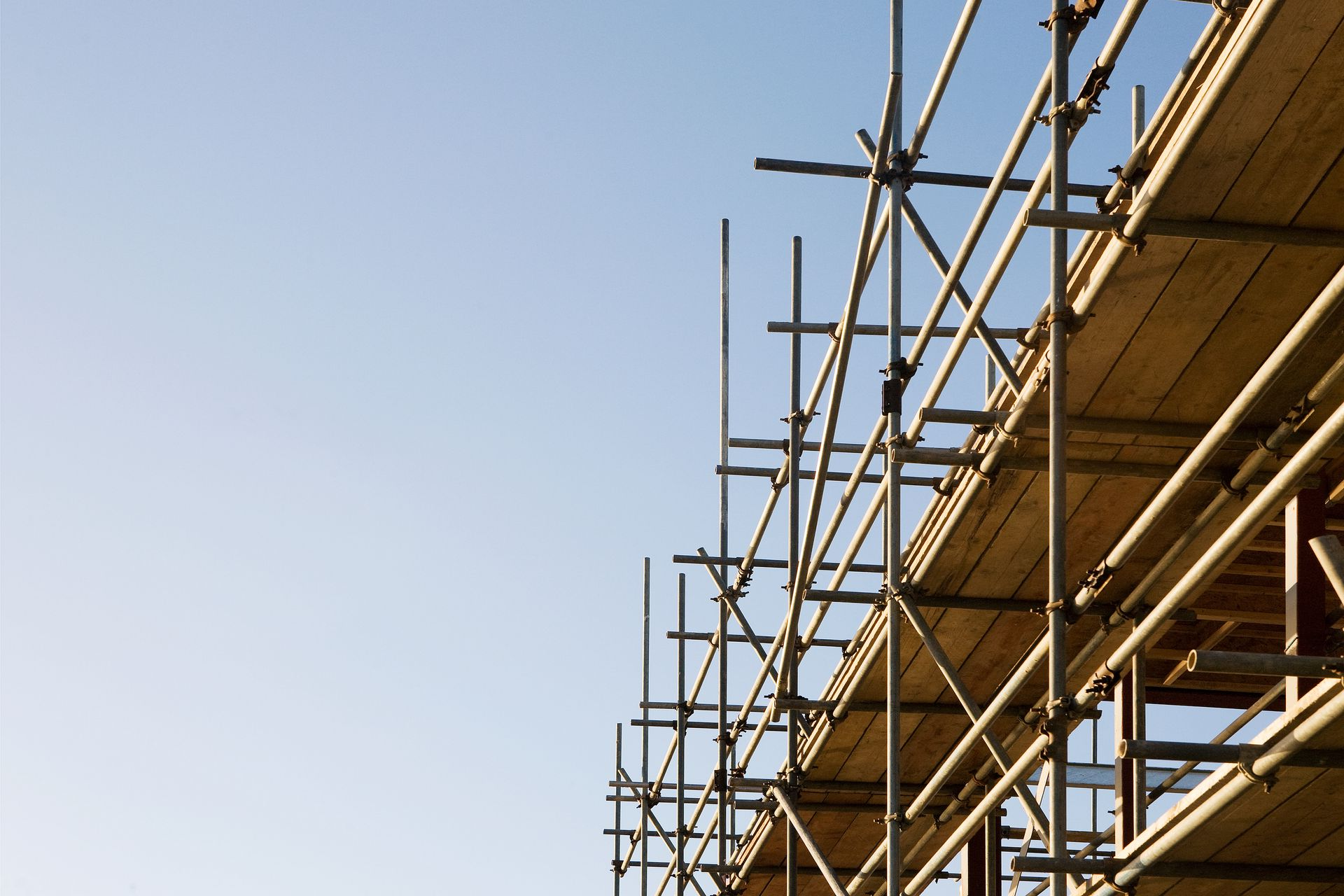 A section of metal scaffolding with wooden planks reaching toward a clear, bright blue sky.