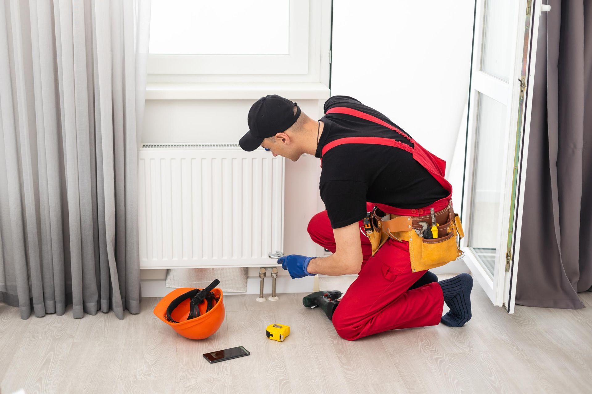 Plumber kneeling by a radiator, tightening a valve with tools on the floor in a bright room
