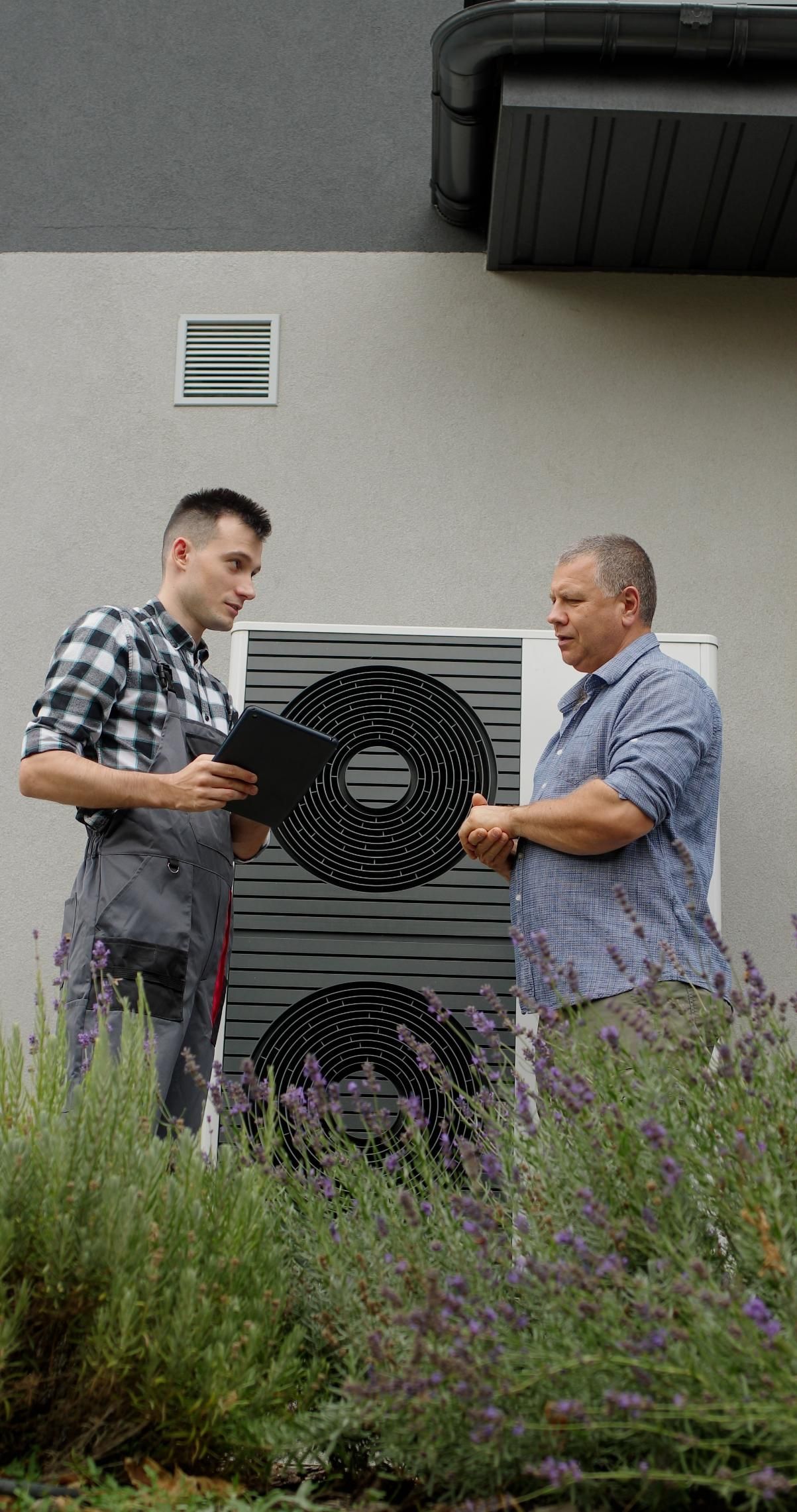 Two men standing by an outdoor air-conditioning unit in front of a building.