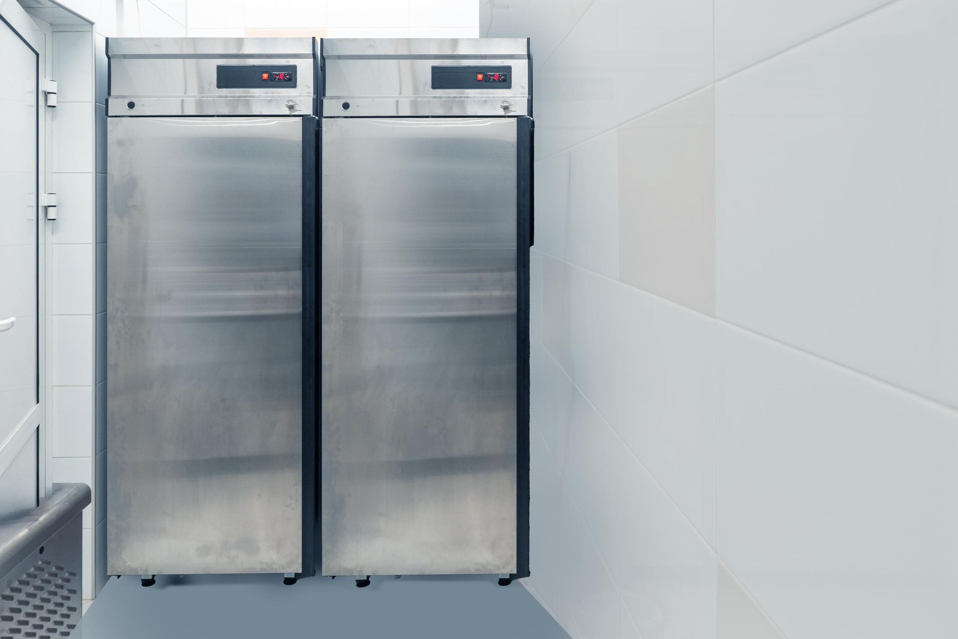 Two stainless steel commercial refrigerators in a bright white room