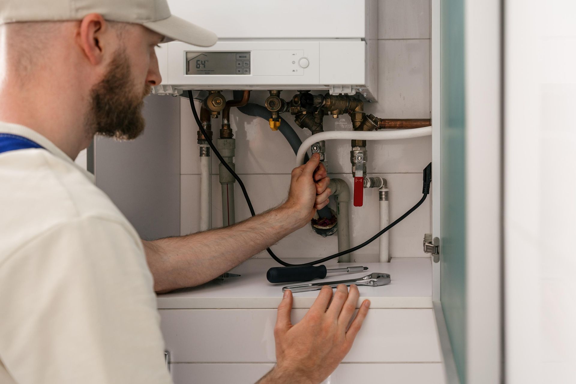 Technician inspecting wiring inside an open boiler cabinet with a wrench in hand