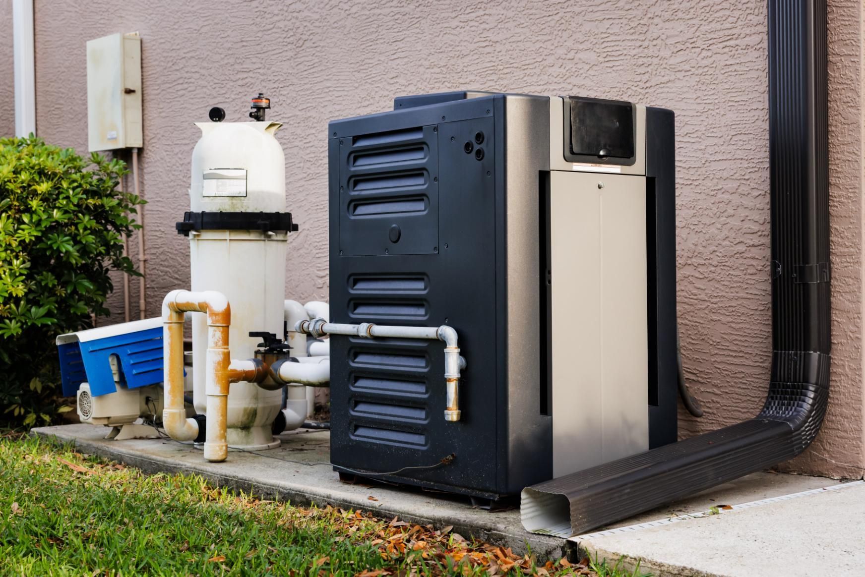 Outdoor HVAC unit beside a house wall with pipes, vents, and a downspout