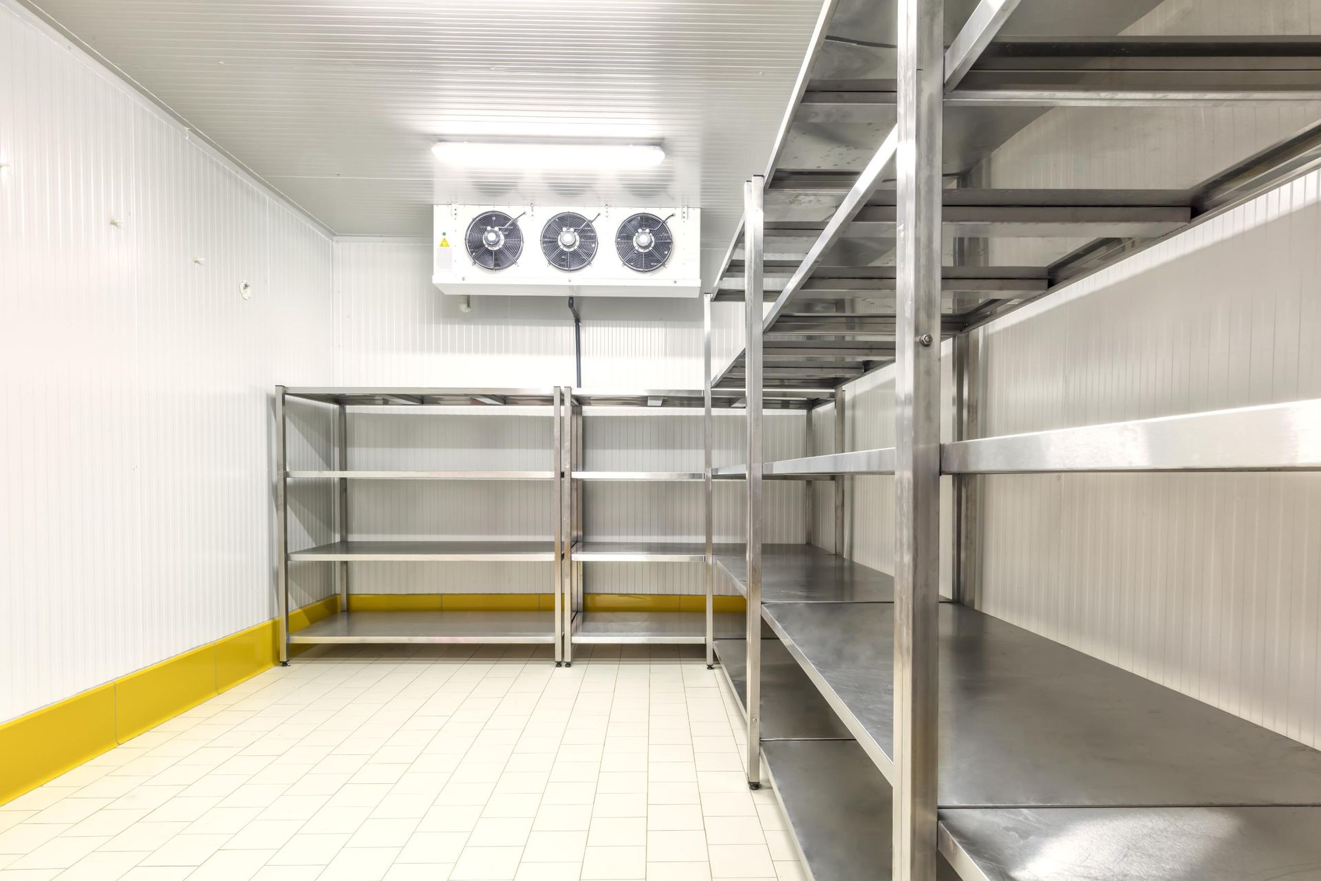 Empty commercial walk-in cooler with metal shelving and wall-mounted fans