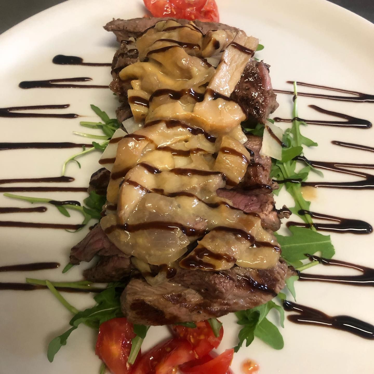 Fettine di bistecca guarnite con funghi e glassa balsamica, servite su un letto di rucola con pomodorini ciliegino.