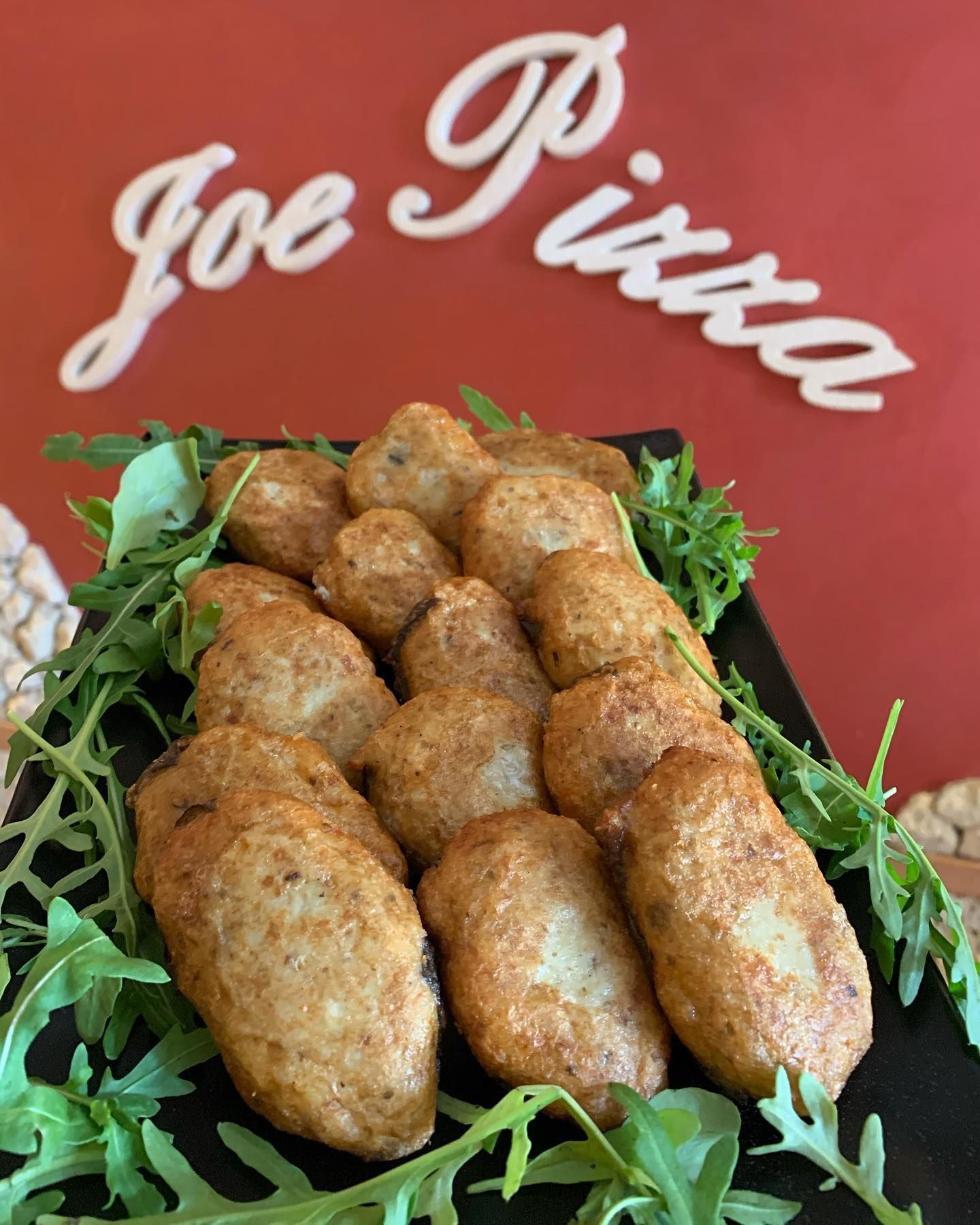Un piatto di palline di pasta fritta dorate, servite su un letto di rucola, posizionato sotto un'insegna rossa con la scritta