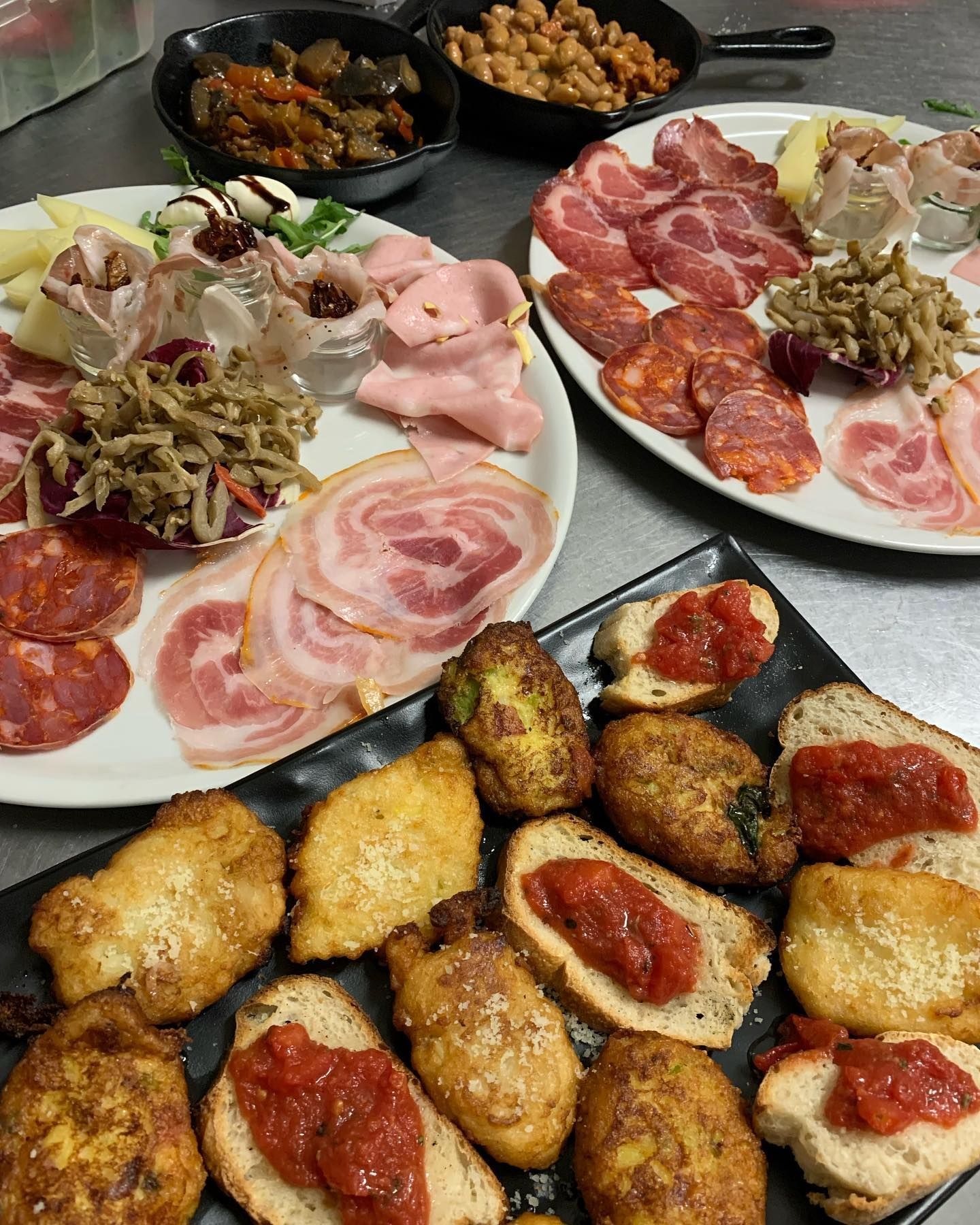 Un assortimento di antipasti italiani con vari salumi, fritture, bruschette e piccole ciotole di contorni.