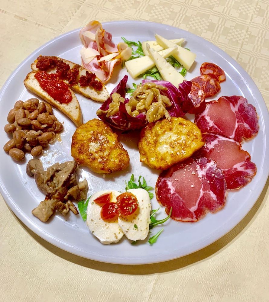 Un assortimento di antipasti italiani, tra cui salumi, formaggi, bruschette, fagioli e verdure cotte, serviti su un piatto.