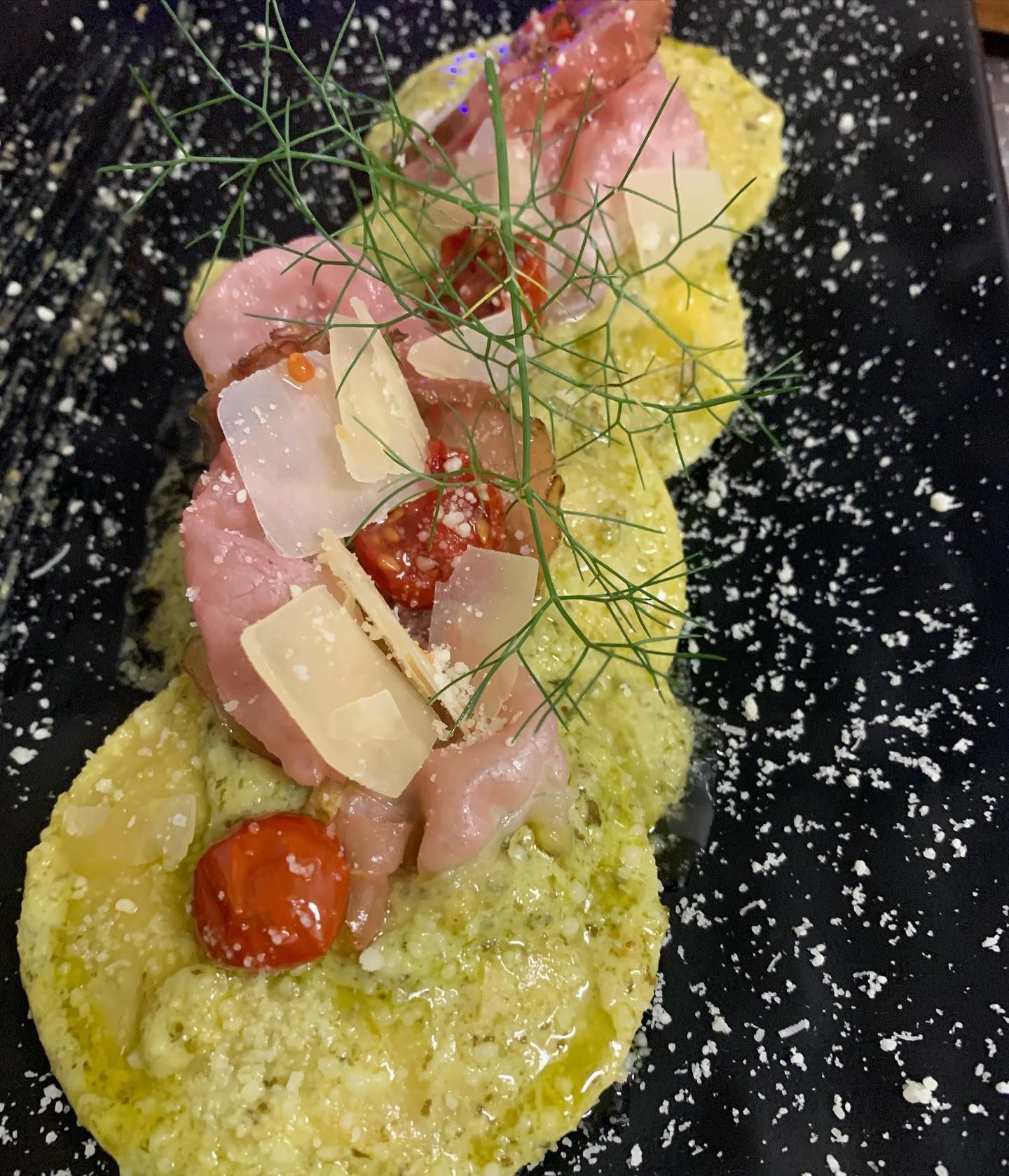 Tre tortine rotonde con pesto, guarnite con prosciutto crudo, pomodori secchi, scaglie di parmigiano e finocchio fresco.